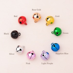 May include: A selection of small, round bells in a range of colours: red, rose gold, gold, green, black, silver, pink, light purple, and sapphire blue. Each bell has a small loop for attachment. Colour names are labelled on the image.
