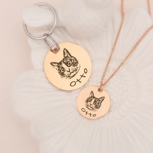 May include: Two gold-toned round pet ID tags with a black and white cat image and the name "Otto" engraved on each. One tag is attached to a silver key ring and the other is on a gold chain.