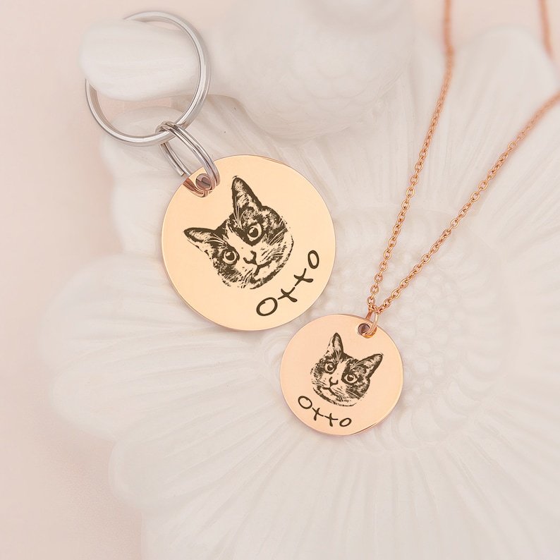 May include: Two gold-toned round pet ID tags with a black and white cat image and the name "Otto" engraved on each. One tag is attached to a silver key ring and the other is on a gold chain.