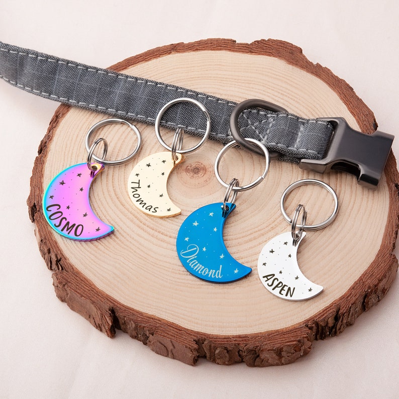 K&ouml;nnte beinhalten: Vier hundemarken in Halbmondform mit gravierten Namen: Cosmo, Thomas, Diamond und Aspen. Jede Marke hat einen silbernen Ring und ein kleines Sternendesign.