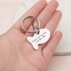 May include: Silver fish-shaped keychain with a split ring. The keychain has the text "Please Call My Mom 123-456-7890" engraved on it.