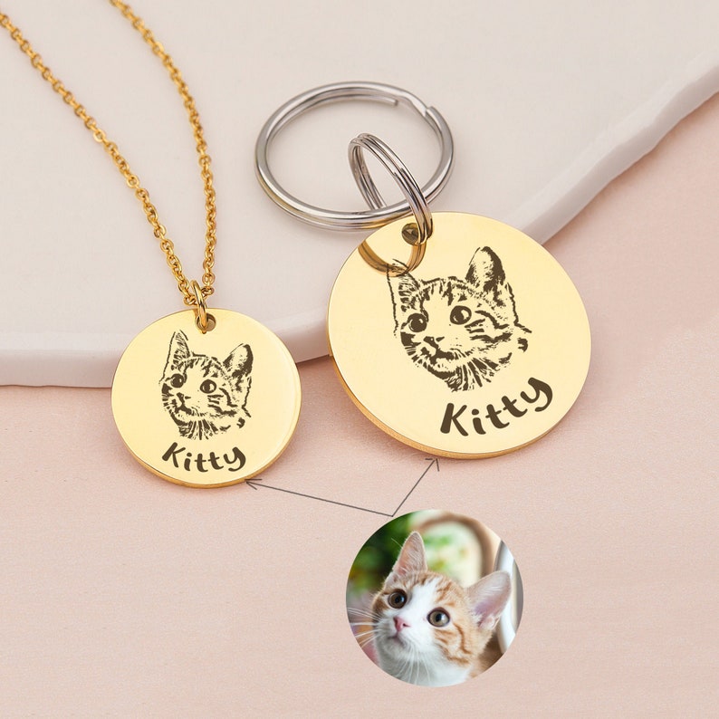 May include: Gold-toned necklace and keychain with round pendants featuring engraved images of a cat and the word "Kitty".