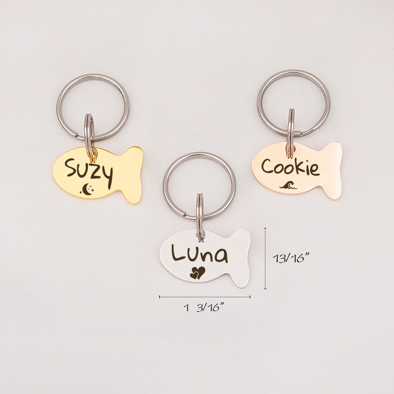 May include: Three gold, silver, and rose gold fish-shaped pet ID tags with key rings. The tags are engraved with the names "Suzy", "Luna", and "Cookie". The tags measure 1 3/16 inches long and 13/16 inches wide.
