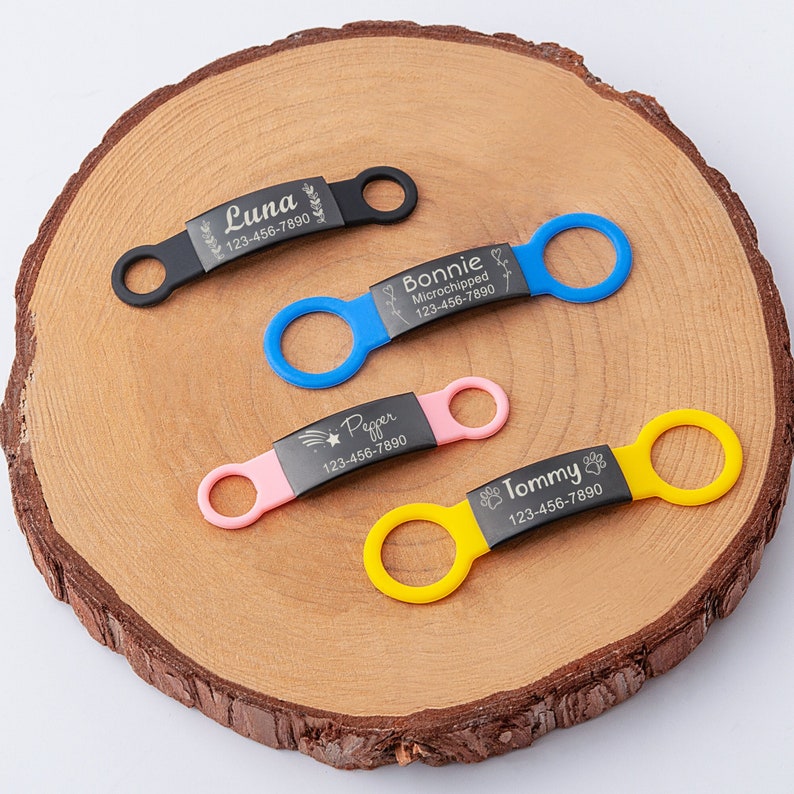 May include: Four personalized dog tags with different colored bands. The tags are engraved with the names Luna, Bonnie Microchipped, Pepper, and Tommy, along with phone numbers.