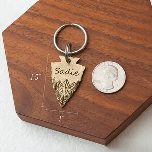 以下が含まれることがあります： 山と「Sadie」という名前が刻まれた、金色の矢じり型のキーホルダー。キーホルダーの高さは1.5インチ、幅は1インチです。