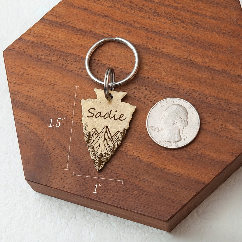 以下が含まれることがあります： 山と「Sadie」という名前が刻まれた、金色の矢じり型のキーホルダー。キーホルダーの高さは1.5インチ、幅は1インチです。