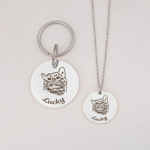 May include: A silver pet ID tag with a black and white engraved image of a cat and the name "Lucky" on a silver chain and a matching keychain.