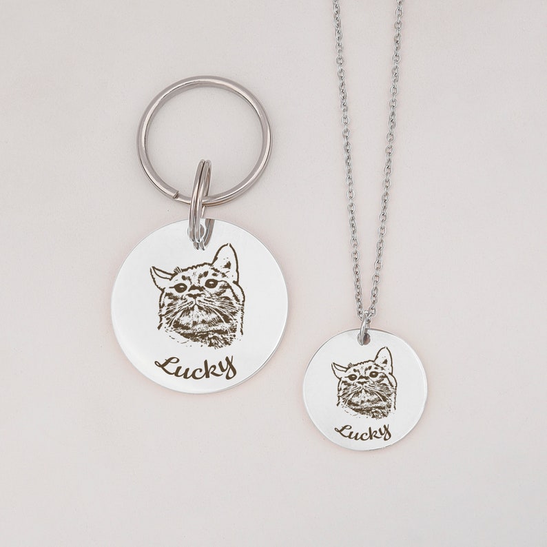 May include: A silver pet ID tag with a black and white engraved image of a cat and the name "Lucky" on a silver chain and a matching keychain.