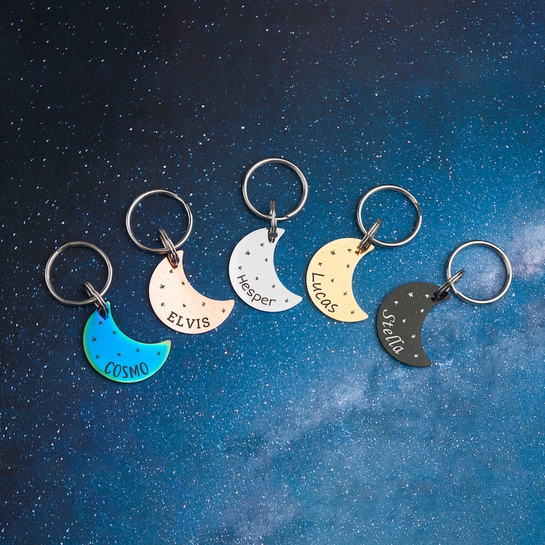 May include: Five silver crescent moon keychains with different colored finishes and engraved names: Cosmo, Elvis, Hesper, Lucas, and Stella.