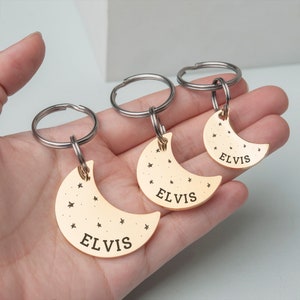 K&ouml;nnte beinhalten: Drei goldene Halbmond-Schl&uuml;sselanh&auml;nger mit dem Namen "ELVIS" auf jedem graviert. Jeder Schl&uuml;sselanh&auml;nger hat einen silbernen Ring und ein kleines Sternendesign.