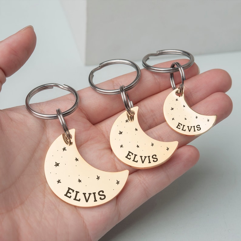 K&ouml;nnte beinhalten: Drei goldene Halbmond-Schl&uuml;sselanh&auml;nger mit dem Namen "ELVIS" auf jedem graviert. Jeder Schl&uuml;sselanh&auml;nger hat einen silbernen Ring und ein kleines Sternendesign.