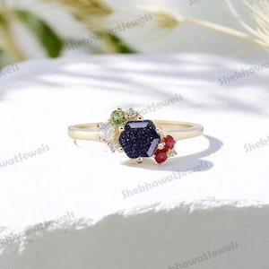 May include: A gold ring with a blue gemstone surrounded by smaller white, green, and red gemstones.