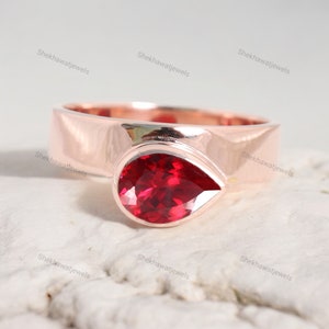 Op de afbeelding: Een ring met een peervormige robijn-edelsteen, gezet in een roségouden band. De ring is simpel en elegant, met een gladde, gepolijste afwerking.