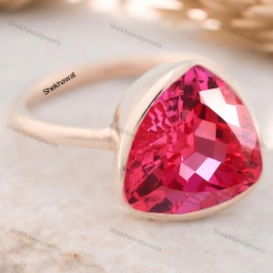 May include: A rose gold ring with a triangular pink gemstone. The ring is set in a bezel setting and has a smooth band.