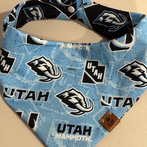 Puede incluir: Bandana azul claro para perros con el logotipo y el texto de Utah Mammoth repetidos. El reverso es negro y blanco. Lleva una etiqueta de cuero marrón. Accesorio para mascotas.