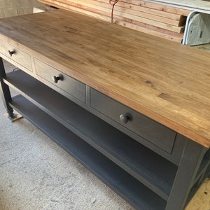 Puede incluir: Una isla de cocina negra con una encimera de madera y tres cajones. La isla tiene dos estantes y patas de metal negro.