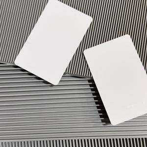 Puede incluir: Dos tarjetas blancas en blanco sobre una superficie gris texturizada. La superficie tiene un patrón repetitivo de líneas en relieve.