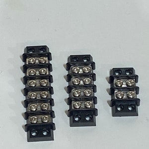 May include: Three black electrical terminal blocks with silver screws. The blocks have different lengths, with the largest block having six screw terminals and the smallest block having three screw terminals.