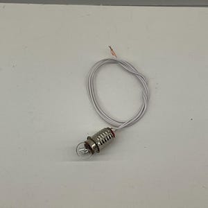 May include: A small, clear light bulb with a silver base and red accents, connected to a white wire. The wire is coiled into a loop. The bulb is designed for electrical applications.