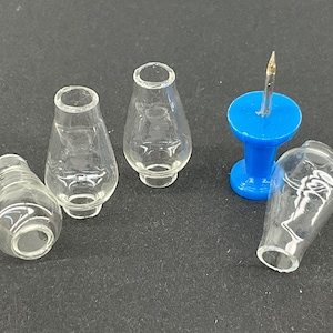 May include: Four small, clear glass lamp chimneys and a blue push pin with a gold pin. The chimneys are teardrop-shaped with a flared top and a rounded base. The push pin has a round head and a sharp pin.