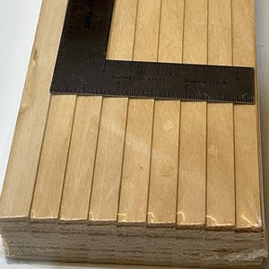 May include: A stack of light-colored wooden craft sticks with a metal stainless steel ruler on top. The ruler is marked with measurements in inches and is made in the U.S.A.