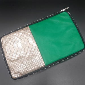 May include: A rectangular clutch with a silver snakeskin pattern on the left and green leather on the right. The clutch has a black zipper and a silver zipper pull. The interior is not visible.