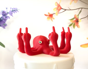 May include: A red octopus figurine with all eight tentacles raised in a middle finger gesture. The octopus is sitting on a white cake.