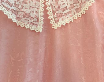 May include: A light pink dress with a white lace collar, hanging on a pink hanger. The dress has a floral pattern and a delicate, vintage aesthetic. The lace collar adds a touch of elegance.