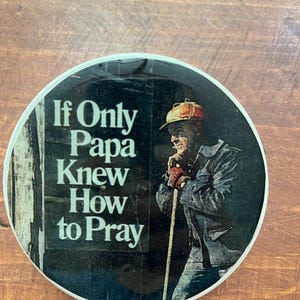 May include: Round coaster with the text "If Only Papa Knew How to Pray" and an illustration of a man in work clothes leaning on a staff. The coaster has a white border and a dark background.