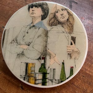 May include: Round coaster with a vintage illustration of two people and bottles. The artwork features a muted color palette with green, yellow, and neutral tones. The coaster is likely made of ceramic or a similar material.