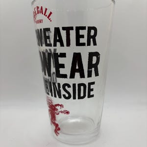 Puede incluir: Vaso de pinta transparente con el texto negro "WEATER WEAR THE INSIDE". El logotipo de Fireball Whisky est&aacute; en la parte superior y un gr&aacute;fico de drag&oacute;n rojo en la parte inferior. El vaso est&aacute; vac&iacute;o.