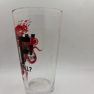 May include: A clear pint glass with a red graphic design. The design includes the letters "F", "H", and "W", along with the question "BALL?" in a stylized font. The glass is empty and sits on a white surface.