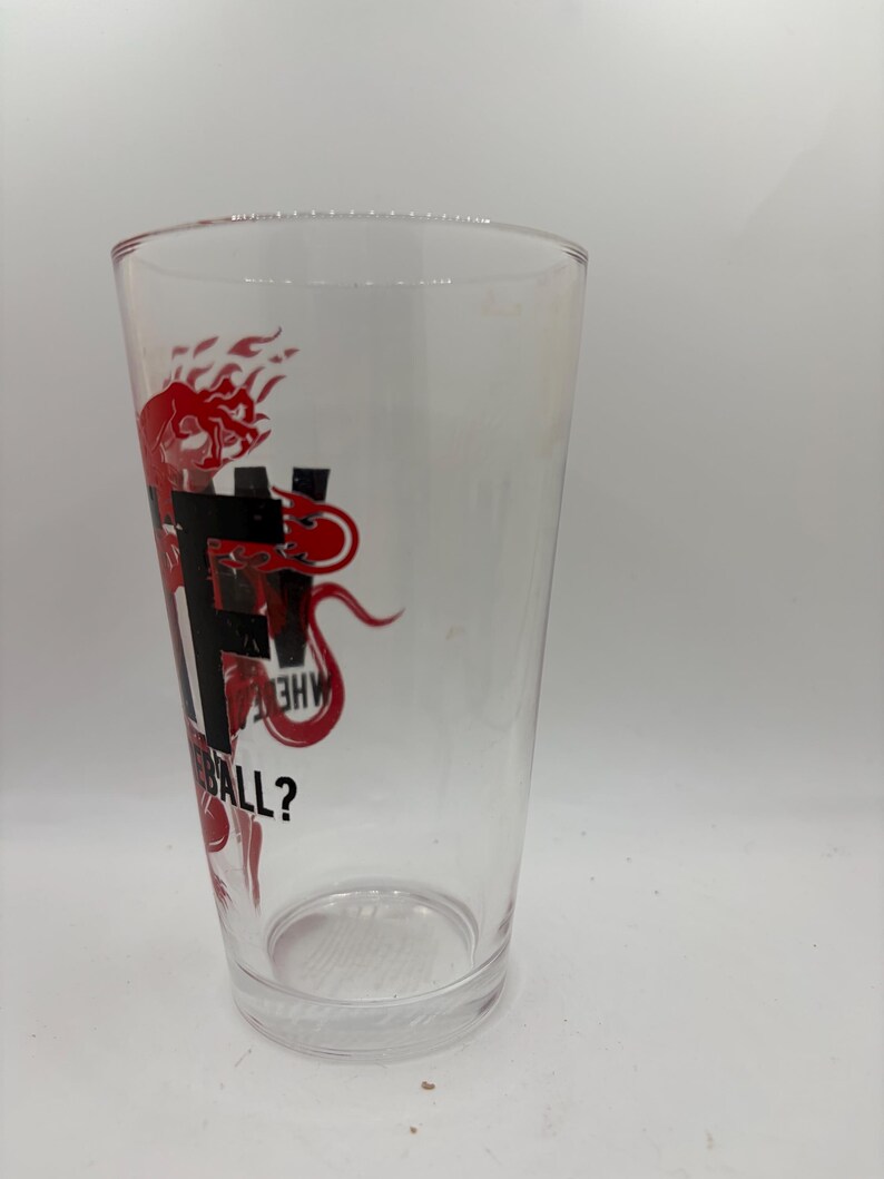 May include: A clear pint glass with a red graphic design. The design includes the letters "F", "H", and "W", along with the question "BALL?" in a stylized font. The glass is empty and sits on a white surface.