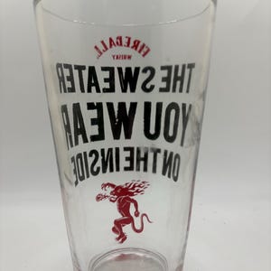 Puede incluir: Un vaso de pinta transparente con las palabras "Fireball Whisky" y "The Sweater You Wear On The Inside" impresas en negro. Tambi&eacute;n hay una ilustraci&oacute;n roja de una criatura m&iacute;tica.