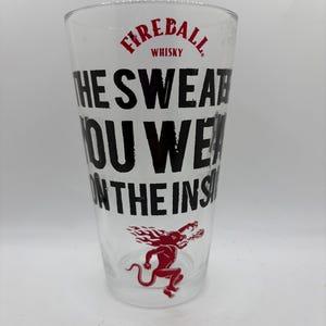 Puede incluir: Un vaso de pinta transparente con el texto "THE SWEAT YOU WEAR ON THE INSIDE" en negro. La palabra "Fireball" y la imagen de un diablo rojo tambi&eacute;n est&aacute;n impresas en el vaso. El vaso es para whisky.
