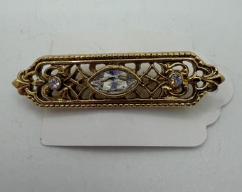 Broche de estilo victoriano en tono dorado con incrustaciones de cristal en forma de marquesa y redonda.