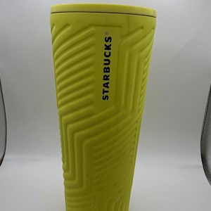 May include: A tall, yellow Starbucks travel mug with a textured geometric pattern. The Starbucks logo is printed in black on the side of the mug. The mug has a lid and is designed to keep beverages hot or cold.