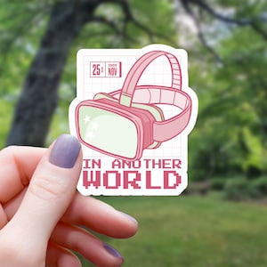 May include: Pink and white sticker with a cartoon VR headset and the text "IN ANOTHER WORLD" in pixelated font. The sticker has a grid pattern in the background and a date stamp that says "25c 1989 NOV".