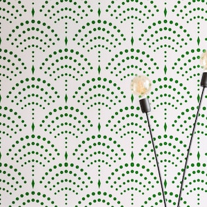 May include: A green and white wall stencil with a repeating pattern of arches made of small dots. The stencil is being used to create a decorative wall design in a room with a red velvet ottoman and a black floor.