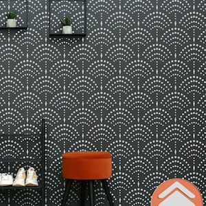 May include: A black and white geometric stencil pattern on a dark gray wall. The stencil features a repeating design of small circles arranged in a curved pattern. A small orange velvet ottoman with black legs sits in front of the wall. The text "Stenciliology" is printed in white on a red arrow pointing upwards.