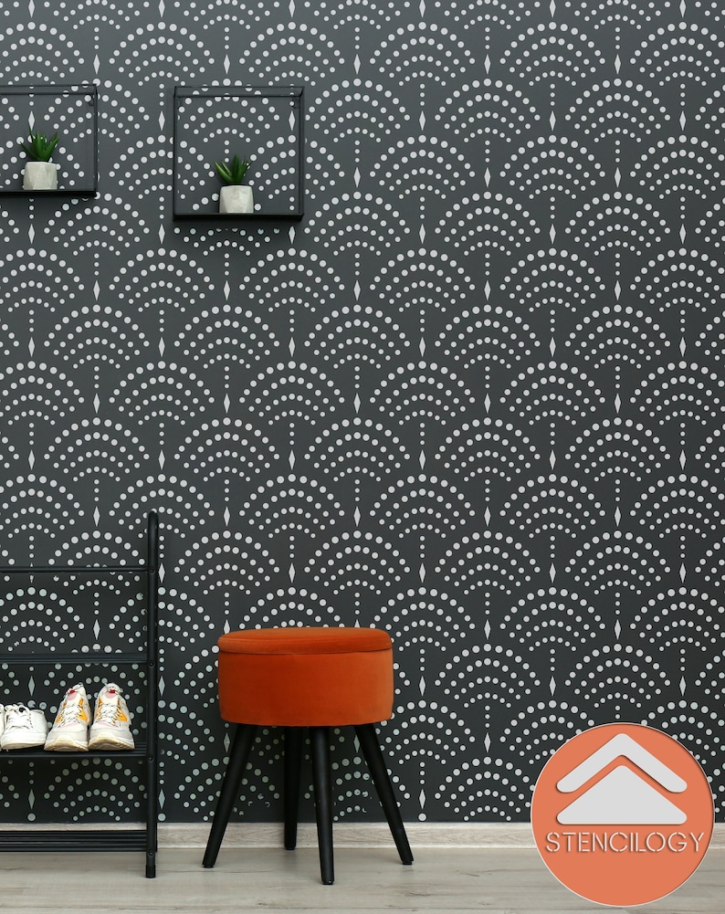 May include: A black and white geometric stencil pattern on a dark gray wall. The stencil features a repeating design of small circles arranged in a curved pattern. A small orange velvet ottoman with black legs sits in front of the wall. The text "Stenciliology" is printed in white on a red arrow pointing upwards.