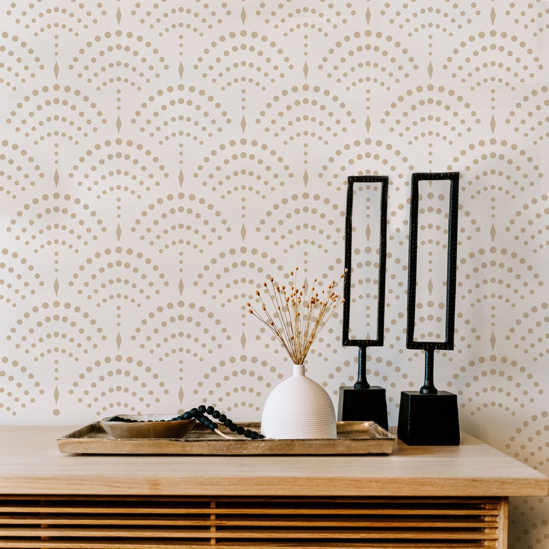 May include: A wooden table with a light wood finish and a decorative tray with two black mirrors, a white vase with dried flowers, and a beaded necklace. The wall behind the table has a white background with a repeating pattern of brown dots and diamonds.