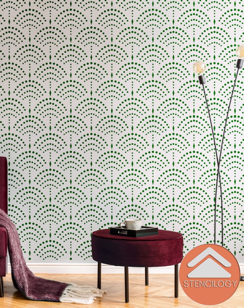 May include: A green and white wall stencil with a repeating pattern of arches made of small dots. The stencil is being used to create a decorative wall design in a room with a red velvet ottoman and a black floor.