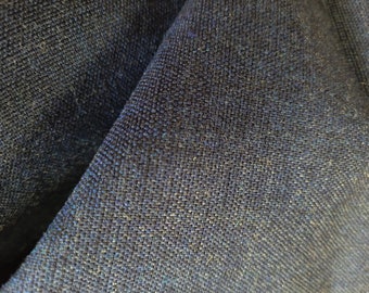May include: Close-up of a textured, dark blue fabric. The weave is visible, with a mix of blue and lighter threads creating a subtle pattern. The fabric is folded, showing depth and texture.