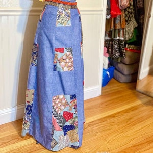 May include: A blue denim skirt with a patchwork design featuring various colors and patterns. The skirt is long and flowing, and it is paired with a yellow and white striped top with a ruffled neckline.