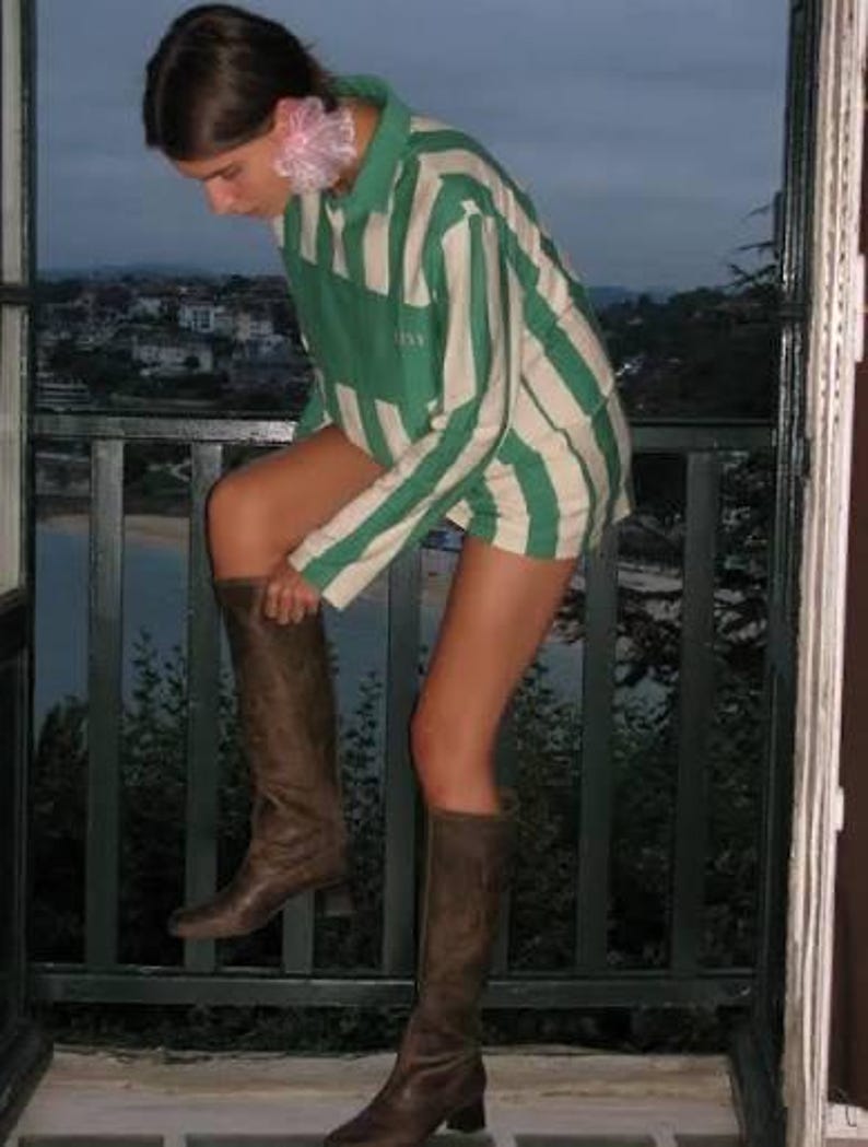 May include: A long-sleeve polo shirt featuring wide vertical stripes in forest green and off-white, paired with knee-high brown leather boots. The shirt has a collar and a button placket, while the boots have a flat sole and a simple, smooth finish.