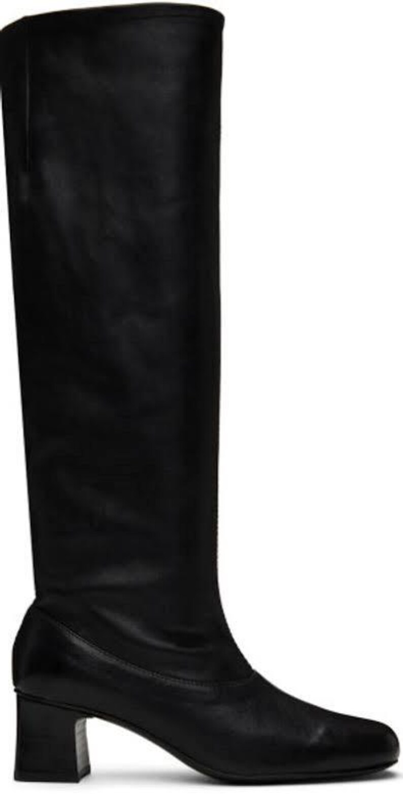 May include: A knee-high black leather boot with a smooth finish and a rounded toe. The boot features a structured shaft that extends to the knee and a sturdy, block-shaped heel. The design is sleek and uniform, showcasing a solid black color.