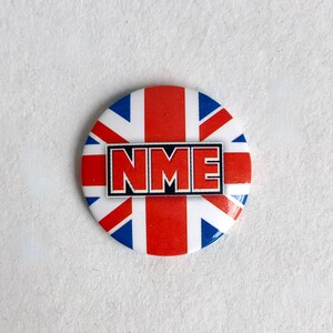 Könnte beinhalten: Ein runder Knopf mit einem rot-weiß-blauen Union-Jack-Design. Die Buchstaben "NME" sind in Schwarz auf dem Knopf gedruckt.