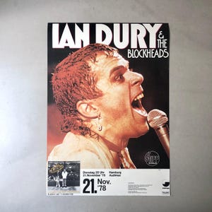 Puede incluir: Un cartel de concierto vintage de Ian Dury & The Blockheads. El cartel muestra a un hombre cantando a un micrófono, con el nombre de la banda en letras blancas. La fecha es el 21 de noviembre del '78.
