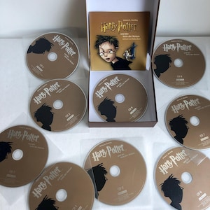 May include: A brown box with a book titled "Harry Potter and the Sorcerer's Stone" and nine audio CDs with the same title. The CDs are in clear plastic sleeves.